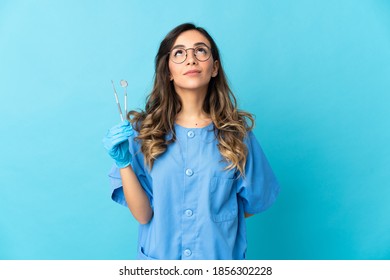 Woman dentist holding tools over isolated on blue background and looking up