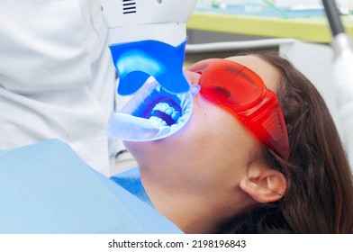 Woman At The Dentist. Relaxed Girl With Closed Eyes And Protective Glasses In The Dentist's Office With Ultraviolet Light.