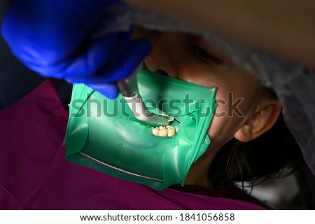 A woman at a dentist's appointment, a dentist uses a rubber dam and dental tools for treatment.