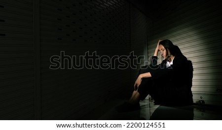 Woman depressed from sad stress pain despair problem, person sit on closed shop on corridor alone with emotion lonely desperate upset head down. Black Dark Underexposure concept, copy space
