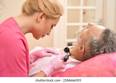 Woman dermatologist examines neoplasms with dermatoscope in man on neck