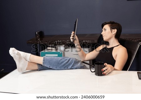 woman at desk in office with feet up looking at tablet