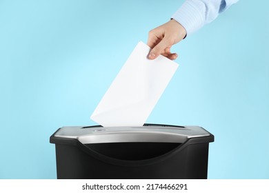 Woman destroying envelope with shredder on light blue background, closeup