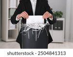 Woman destroying sheet of paper with shredder in office, closeup