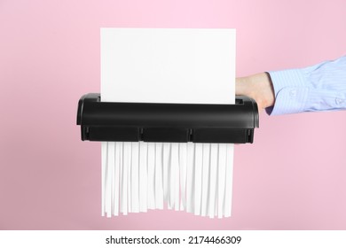 Woman destroying sheet of paper with shredder on pink background, closeup