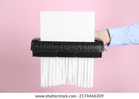 Woman destroying sheet of paper with shredder on pink background, closeup