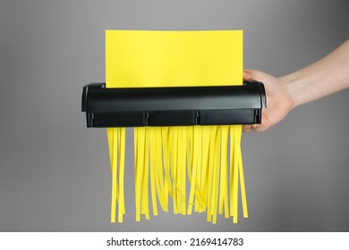 Woman destroying sheet of yellow paper with shredder on grey background, closeup