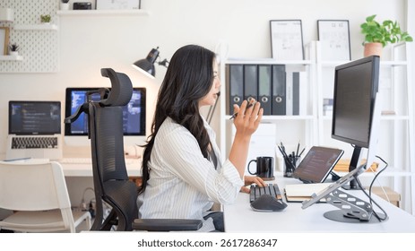 Woman developer writing and reviewing code on several monitors, working efficiently in a clean and organized workspace.