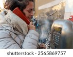 Woman dialing a number on a public telephone booth in the bustling city, bundled in a coat and scarf against the cold winter air