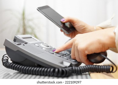 Woman Is Dialing On Land Line Phone And Looking On Mobile Phone