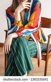 woman in a different colored blouse and trousers sits on a chair, details of clothes