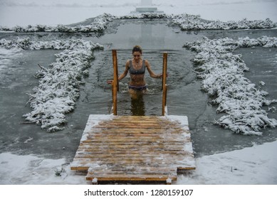 A Woman Is Dipped Into A Hole In The Shape Of A Cross. A Woman Comes Out Of The Icy Water. The Rite Of Washing On The Eve Of The Feast Of The Epiphany. Ukraine. Belogorodka. January 18, 2018