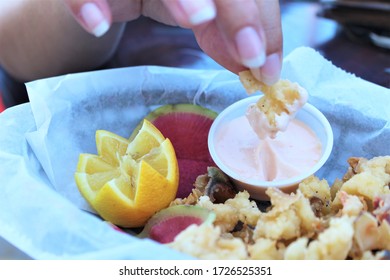 A Woman Dipping Cracked Conch Into Conch Dipping Sauce