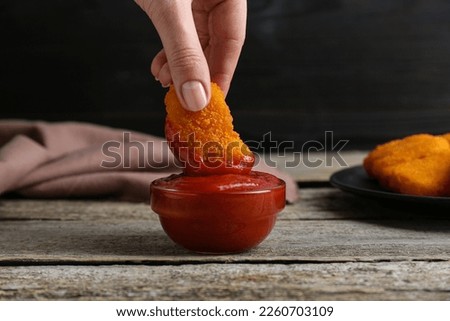 Woman dipping delicious chicken nugget into ketchup at wooden table, closeup