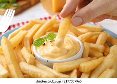 Woman dipping delicious French fries into cheese sauce, closeup
