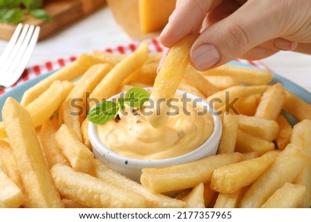 Woman dipping delicious French fries into cheese sauce, closeup