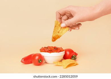 Woman dipping nacho into tasty salsa sauce on color background - Powered by Shutterstock