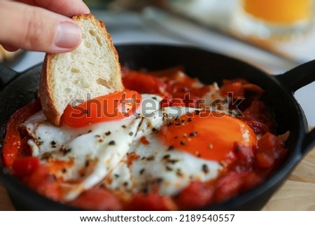 Woman dipping piece of bread into egg yolk, closeup. Eating tasty Shakshouka