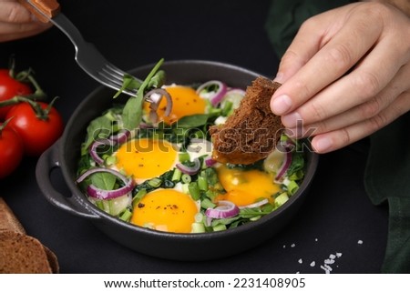 Woman dipping piece of bread into egg yolk, closeup. Eating tasty Shakshuka