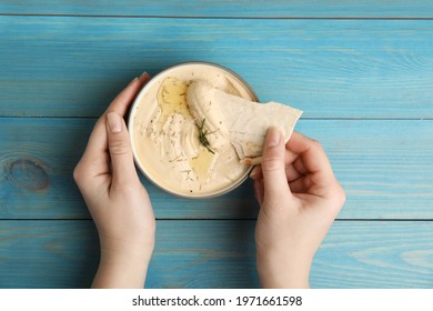 Woman Dipping Pita Chip Into Hummus At Turquoise Wooden Table, Top View