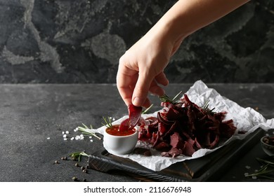 Woman Dipping Spicy Beef Jerky Into Sauce In Bowl On Dark Background