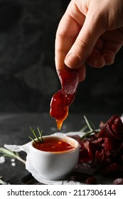 Woman Dipping Spicy Beef Jerky Into Sauce In Bowl On Dark Background