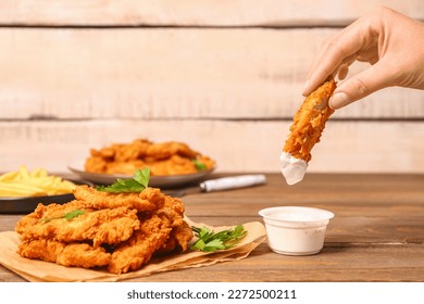 Woman dipping tasty nugget into sauce on wooden table