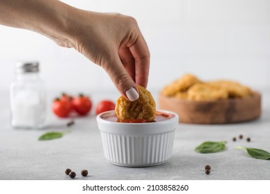 A woman dips a slice of chicken nuggets in ketchup on a light background.