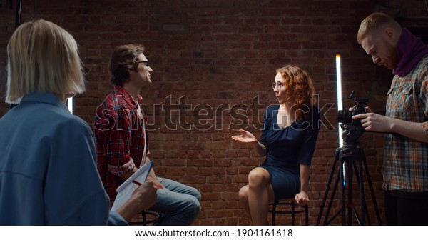 Woman director\
talking to host and guest in studio before filming interview.\
Reporter and interviewed man listening to producer explaining\
details before shooting tv\
show