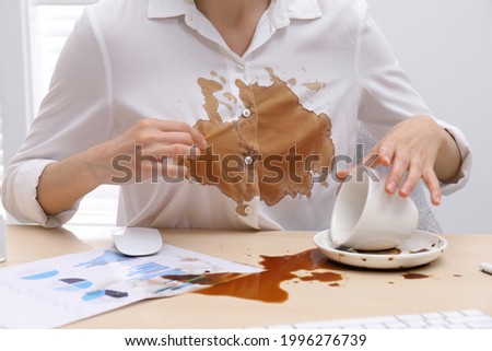 Woman in dirty shirt at wooden desk with coffee spill, closeup