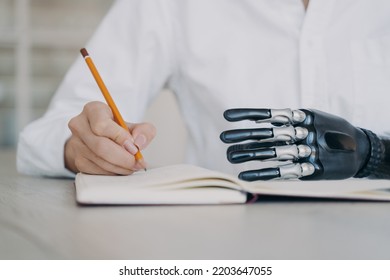 Woman With A Disability Writing With Pencil In Notebook, Close-up. Young Woman With Disability Notes In Notepad, Makes To-do List, Using Bionic Prosthetic Arm, Artificial Robotic Limb.