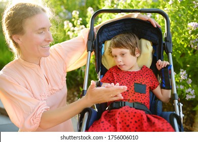 Woman with disabled girl in a wheelchair walking in the summer park. Child cerebral palsy. Disability. Inclusion. Means of rehabilitation. Orthosis. Family with disabled kid.