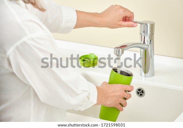 Woman dish washing a thermos bottle with tap\
water in the kitchen close-up on running water, processing a thermo\
bottle.