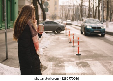 Woman with disposable cup in warm clothing standing in city street in winter