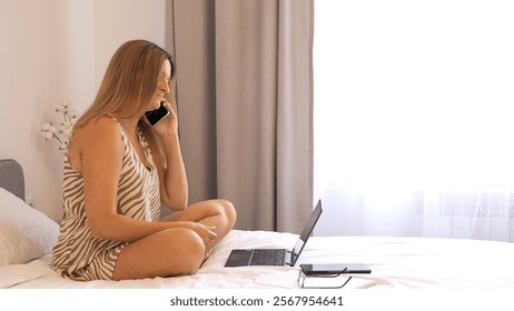 Woman distracted from work answers phone call while typing on laptop in cozy bedroom Phone call interrupts workflow showcasing multitasking challenges and balancing work with unexpected calls - Powered by Shutterstock