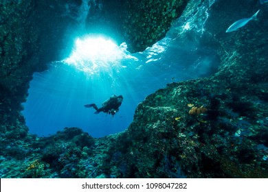 woman diver underwater at the entrance of a cave with sunrays 