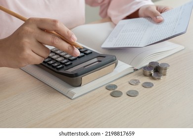 Woman Do Home Accounting And Calculating Book Bank Statement For Household Expense And Money Coins On The Table. Home Accounting Plan For Monthly Payment. Saving And Accounting Concept At Home.