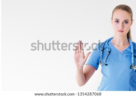 Woman doctor blonde young light gray background studio day beautiful one stethoscope pink purple lilac clothing protests hands forward and keeps feet free stop.