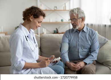 Woman Doctor Cardiologist Or Physician Checking High Blood Pressure Examining Old Male Patient Using Tonometer During Home Medical Care Visit. Elderly Hypertension Cardiovascular Problems Concept.