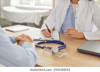 A woman doctor in a clinic takes notes after examining a patient, close-up. There is a stethoscope on the table. Concept of medic appointment, referral for tests, disease treatment strategy - Powered by Shutterstock