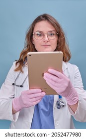 Woman Doctor With A Digital Tablet Apple IPad In A White Uniform On A Blue Studio Background - Moscow, Russia, August 12, 2021