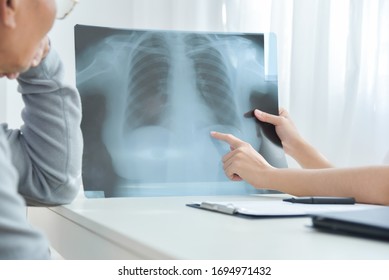 Woman Doctor Discussing About Problem In Lung Disease Of Asian Elderly Patient. Senior Male And Female Physician Looking And Examining X-ray Film In Hospital. Coronavirus, Cancer Illness, Healthcare.