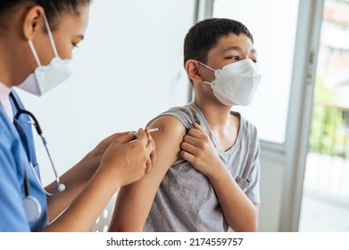 Woman Doctor Giving First Dose Of Covid Vaccine To Little Boy In Clinic Office.Vaccinating Children Against Coronavirus Concept.