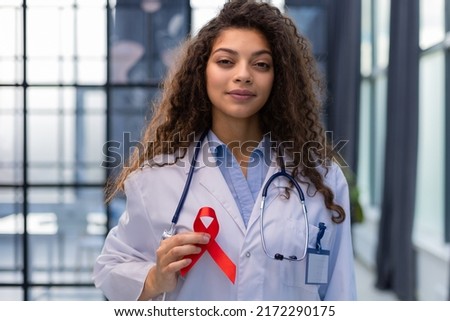 Woman doctor holding a red ribbon in her hand an international day of protecting people from cancer by symbol of struggle and survival mankind.
