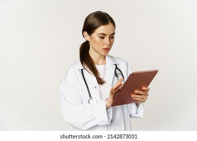 Woman Doctor Looking Concerned At Digital Tablet, Reading With Worried Face Expression, Wearing White Coat, Standing Over White Background