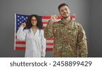 A woman doctor and a man soldier with raised fists in front of an american flag indoors