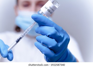 Woman doctor in a mask fills the syringe with medicine from the bottle while preparing to give an injection. Doctor's hands with syringe close-up. COVID-19 coronavirus vaccination concept. - Powered by Shutterstock