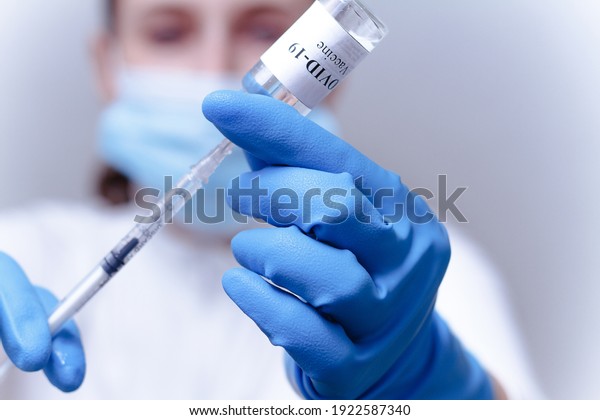 Woman\
doctor in a mask fills the syringe with medicine from the bottle\
while preparing to give an injection. Doctor\'s hands with syringe\
close-up. COVID-19 coronavirus vaccination\
concept.