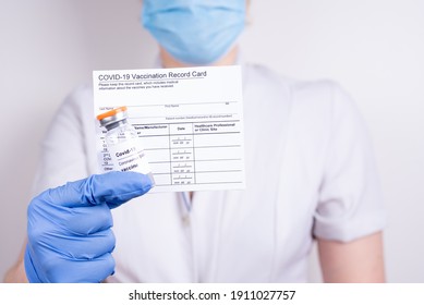 A Woman Doctor In A Mask And Gloves Holding A Vial With Covid-19 Vaccine And Vaccination Record Card, Close Up. Coronavirus Vaccination Concept.