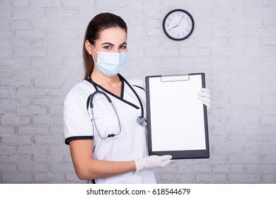 Woman Doctor In Mask Holding Clipboard With Blank Paper In Office